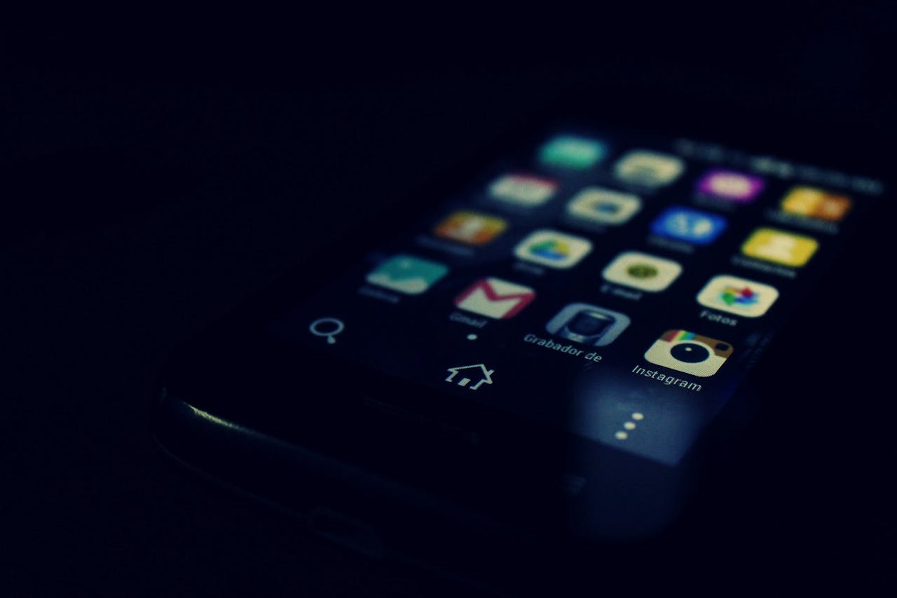 services-01 Dark-themed close-up of a smartphone screen highlighting various apps and touchscreen technology.